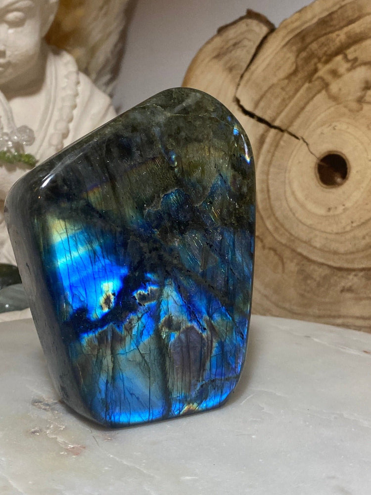 Labradorit - Edelsteine mit besonderer Wirkung. Labradorit-Stein auf Marmorplatte mit Holz im Hintergrund.