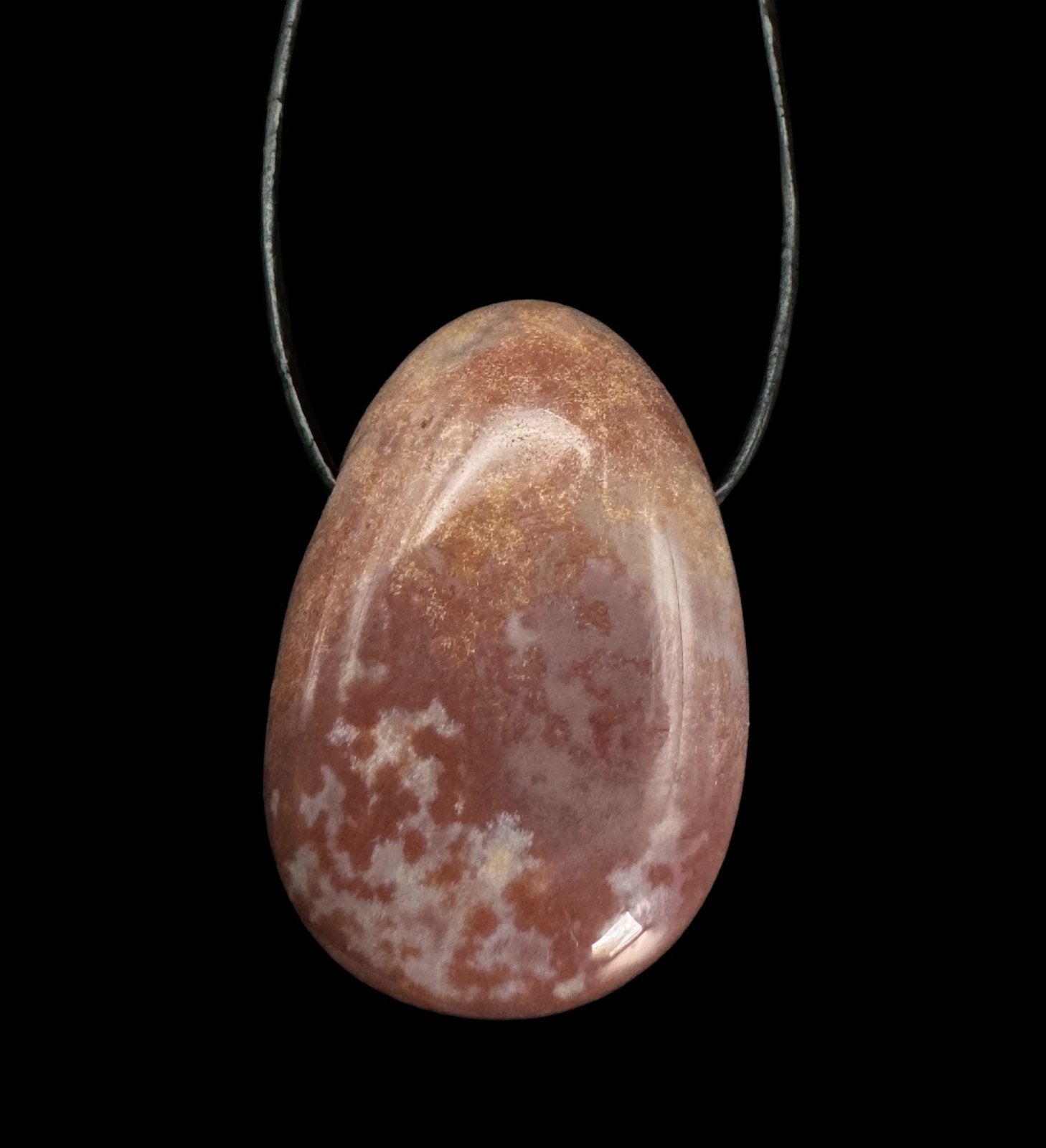 Rotbrauner Sardonyx Heilstein Drop Shape an einem Lederband vor schwarzem Hintergrund